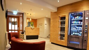 Een hotellobby met een receptiebalie, een automaat en een rode stoel.