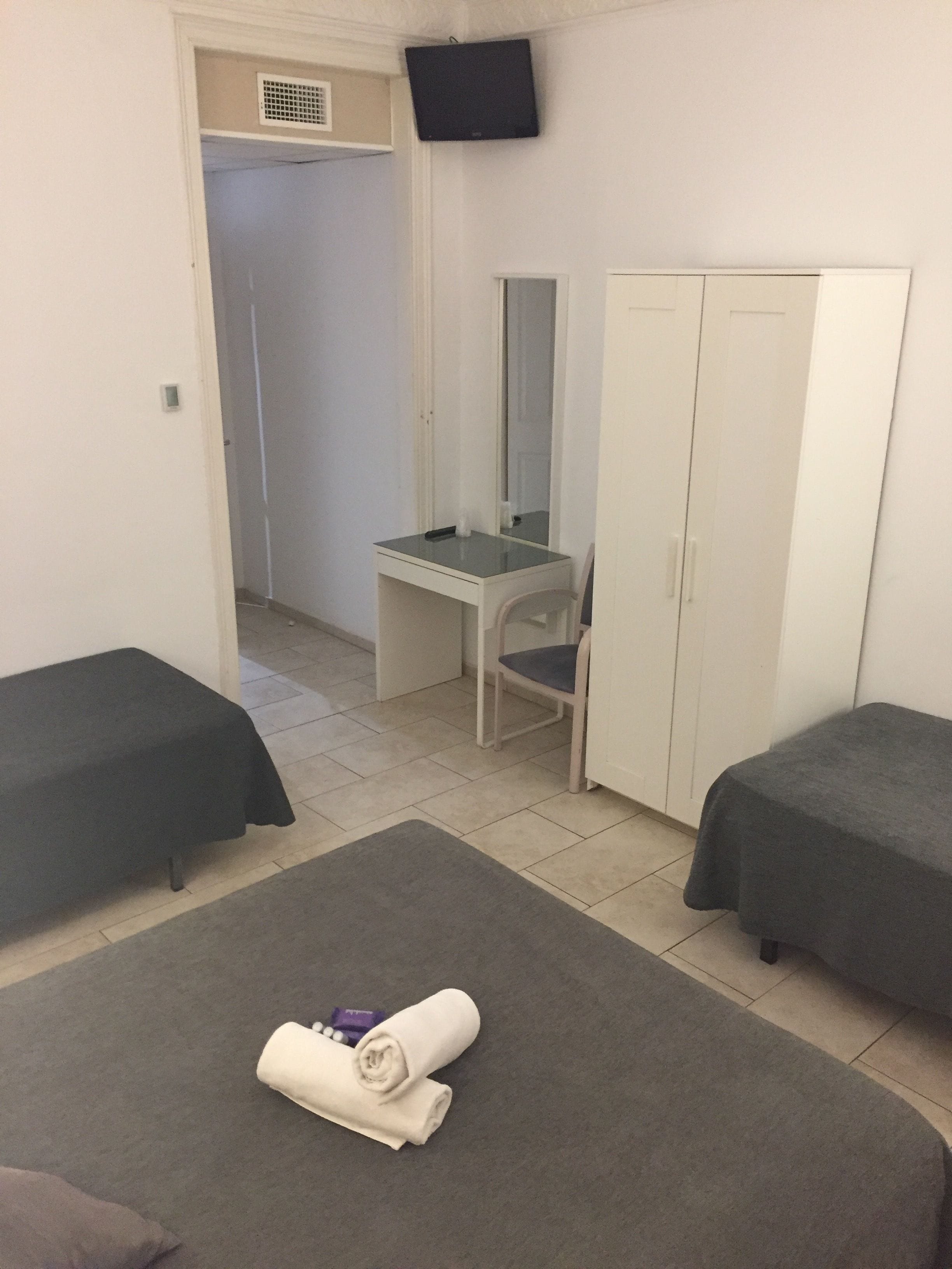 A room with two beds, a desk with a chair, a wardrobe, and a television on the wall.