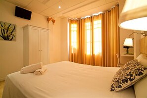 A hotel room with a bed, a TV mounted on the wall, a bedside lamp, and a window with curtains. - Hostal Martinval (Barcelona)