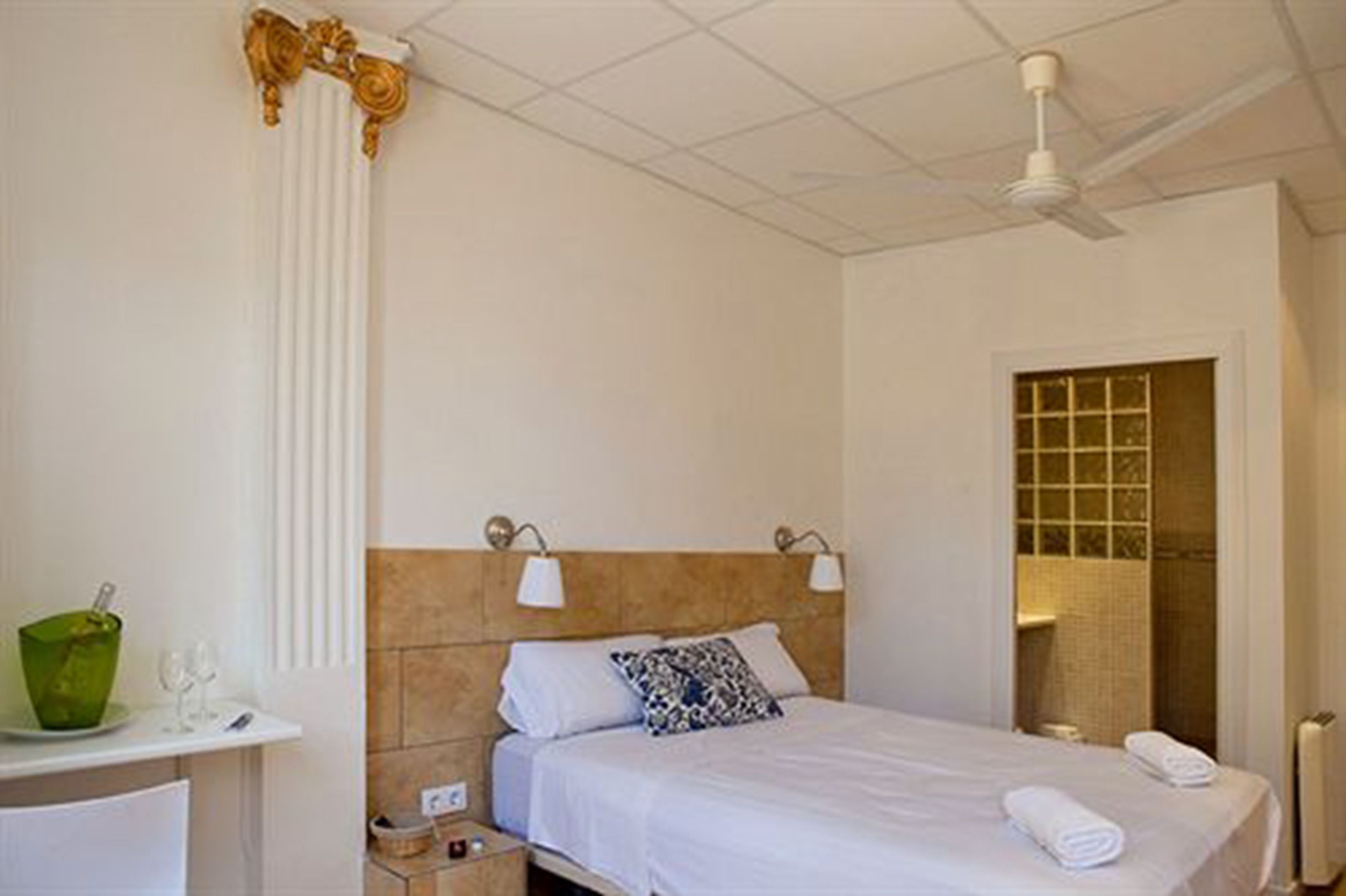 A hotel room with a bed, bedside lamps, a green vase, and a window with a view.