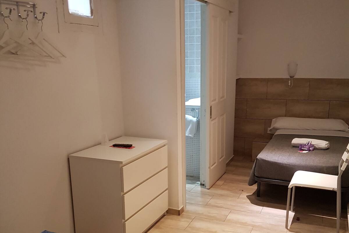Una habitación pequeña y limpia con cama, silla, escritorio y ventana.