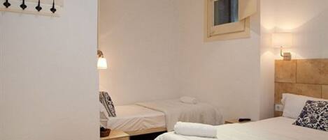 A hotel room with two single beds, a wooden headboard, a bedside table, a nightstand, a lamp, and a window with curtains.