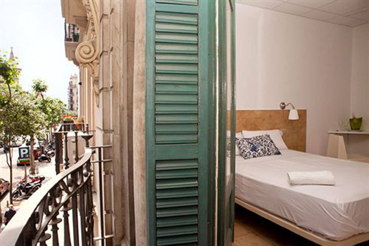 Un dormitorio con una cama, una mesita de noche y una ventana con vista a la calle.
