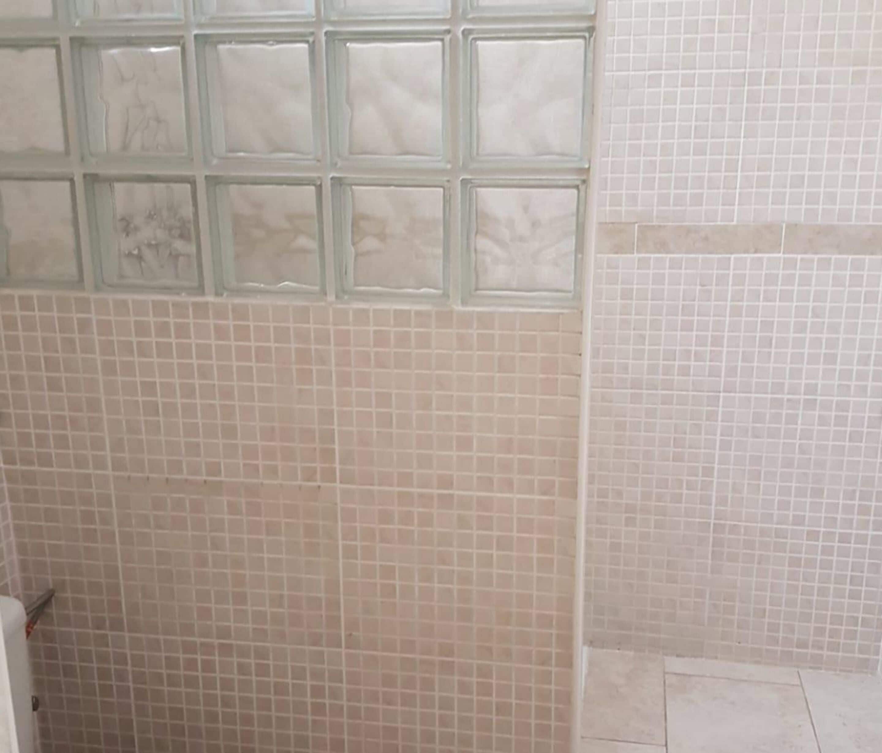Un baño con azulejos color beige, una ventana de vidrio bloqueado y un inodoro blanco.