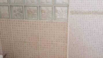 Un baño con azulejos color beige, una ventana de vidrio bloqueado y un inodoro blanco.