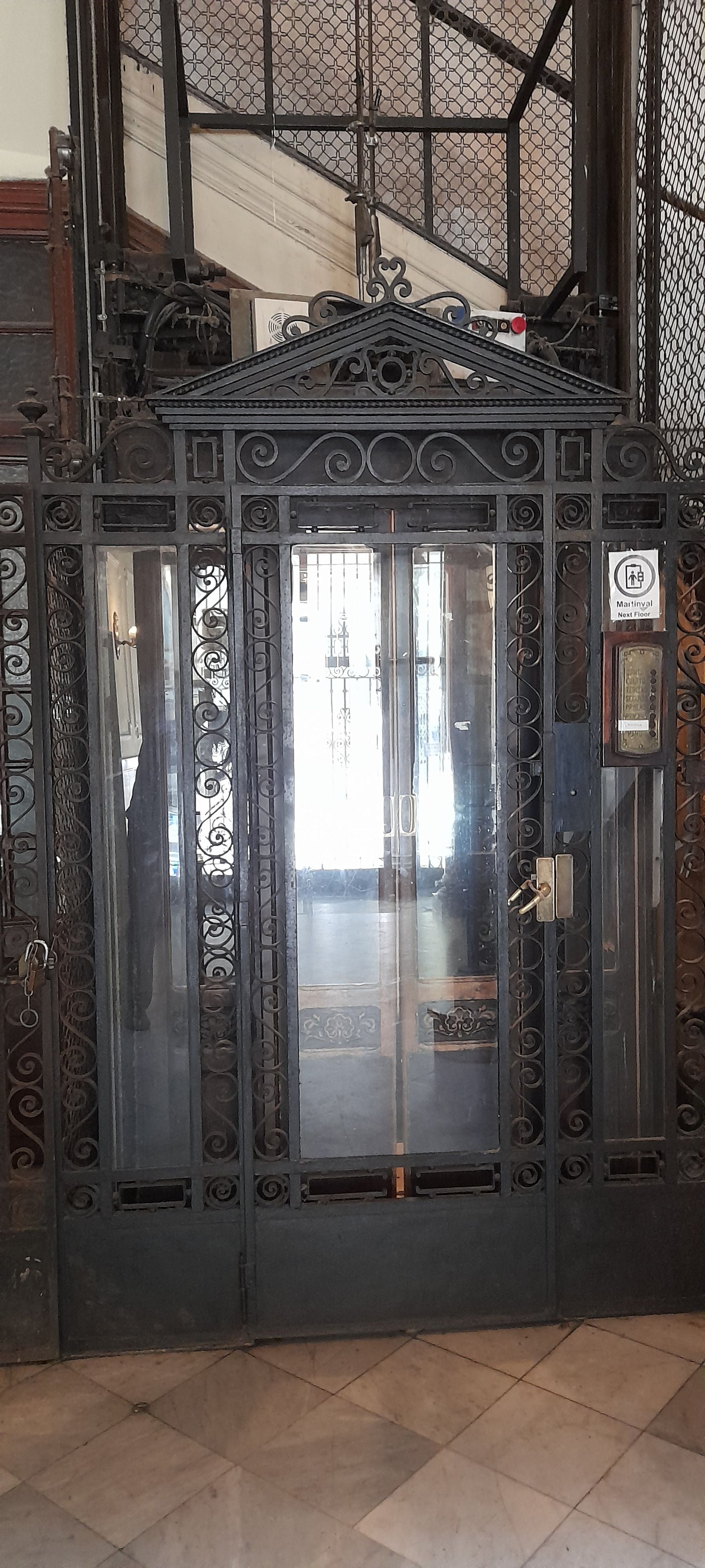 A metal gate with intricate designs and a sign indicating 'Maitinval Next Floor.'