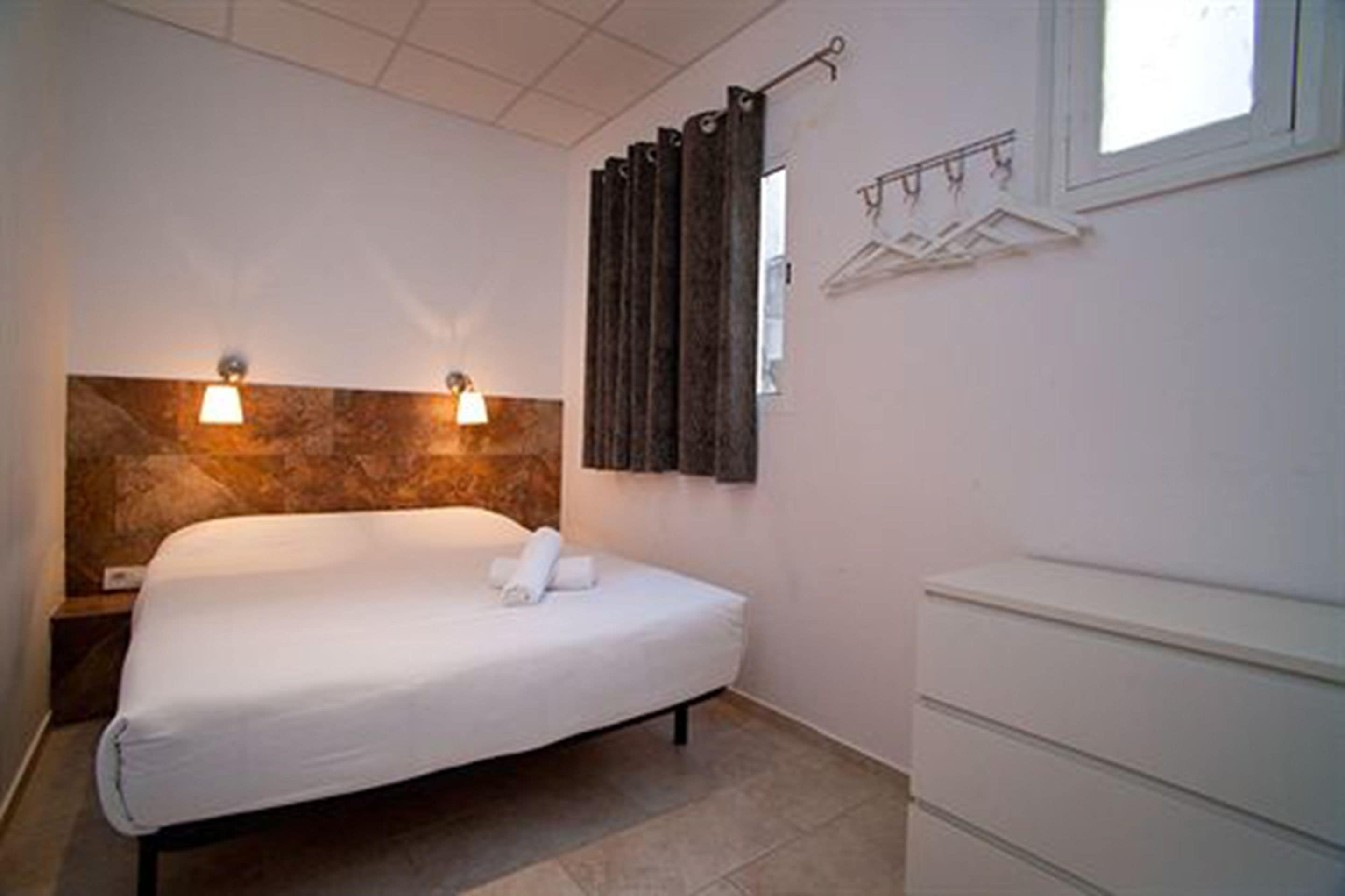 Una habitación de hotel con cama, mesita de noche, cómoda y ventana con cortinas.