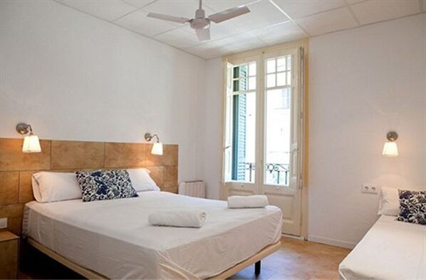 A bedroom with a bed, bedside lamps, a ceiling fan, and a window with shutters. - Hostal Martinval (Barcelona)