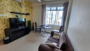 A living room with a TV, sofa, dining table, and a window with curtains. - Hotel Octave (Malé)