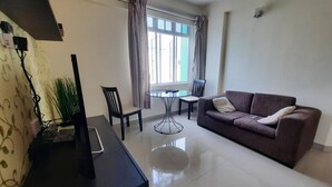 A living room with a sofa, a dining table with chairs, a TV on a stand, and a window with curtains. - Hotel Octave (Malé)