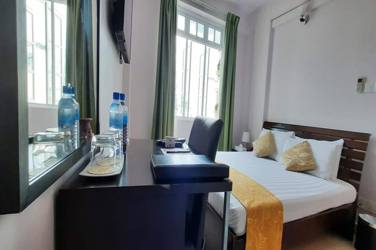 Ein Hotelzimmer mit Bett, Schreibtisch mit Stuhl, Fenster mit Vorhängen und Nachttisch mit Lampe.
