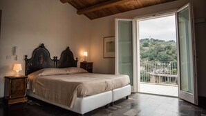 A bedroom with a bed, bedside lamps, a wooden ceiling, and a balcony with a view of greenery.