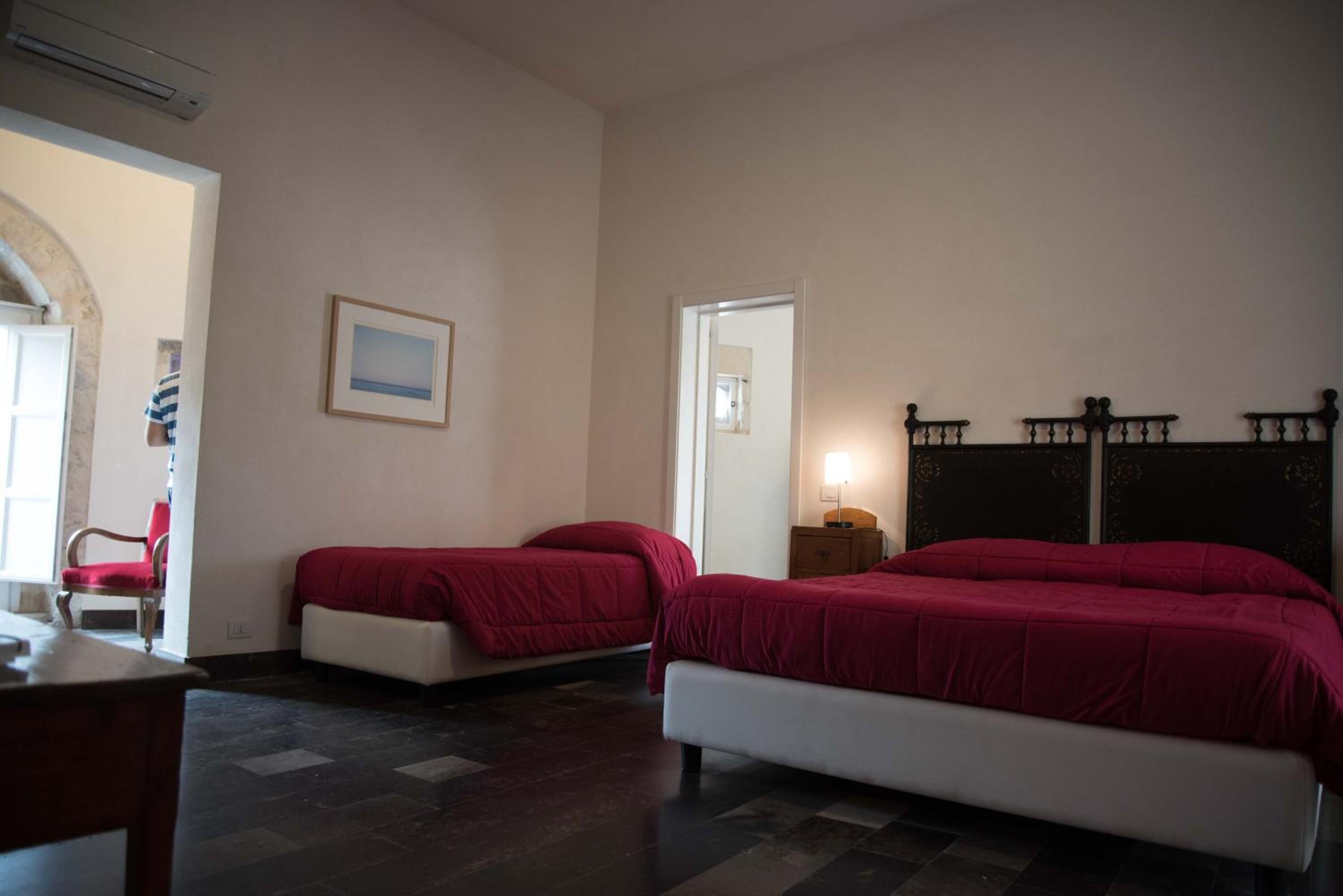 A bedroom with two beds, a desk, a chair, and a small bedside table with a lamp.