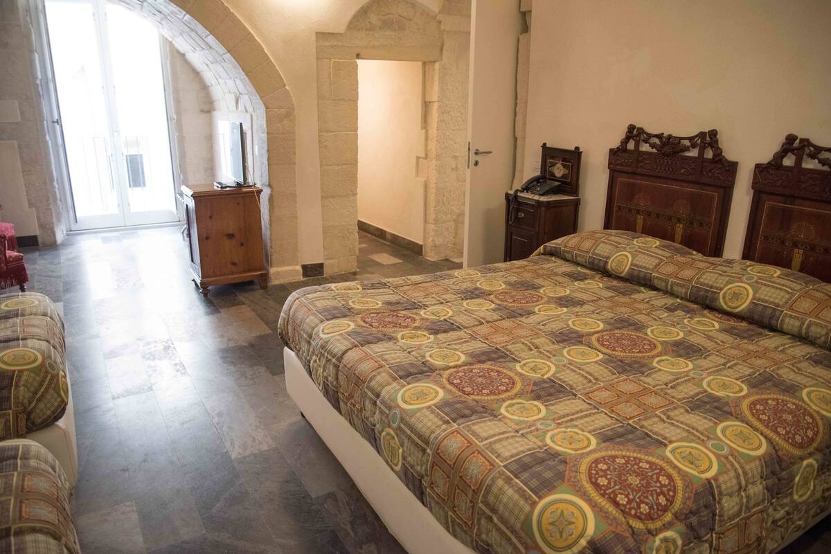 A bedroom with a large bed, a wooden wardrobe, and a television on a cabinet.