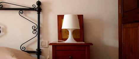 Una cama con cubierta color beige, una mesita de noche con lámpara blanca y una mesita auxiliar de madera con un cajón.
