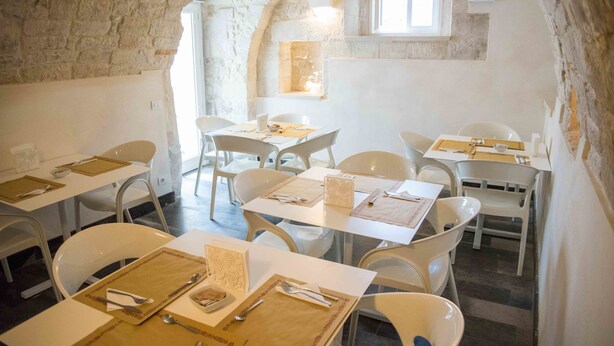 A dining area with white tables and chairs, stone walls, and a small window.