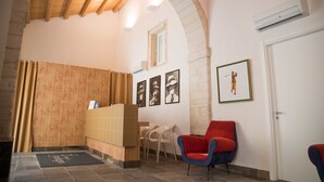 A reception area with a wooden ceiling, a reception desk, a red and blue chair, a small table, and a door.