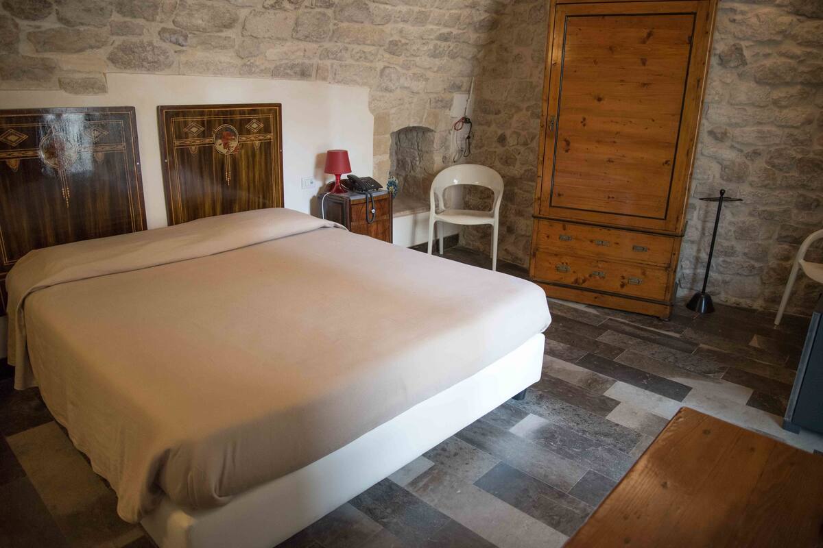 A bedroom with a bed, a wooden wardrobe, a white chair, and a small table.
