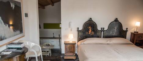 A bedroom with a large bed, a desk with a chair, a bedside table with a lamp, and a painting on the wall.