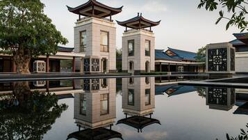 Un edificio tradicional con dos torres al estilo pagoda, una superficie acuática reflectante y un árbol en primer plano.