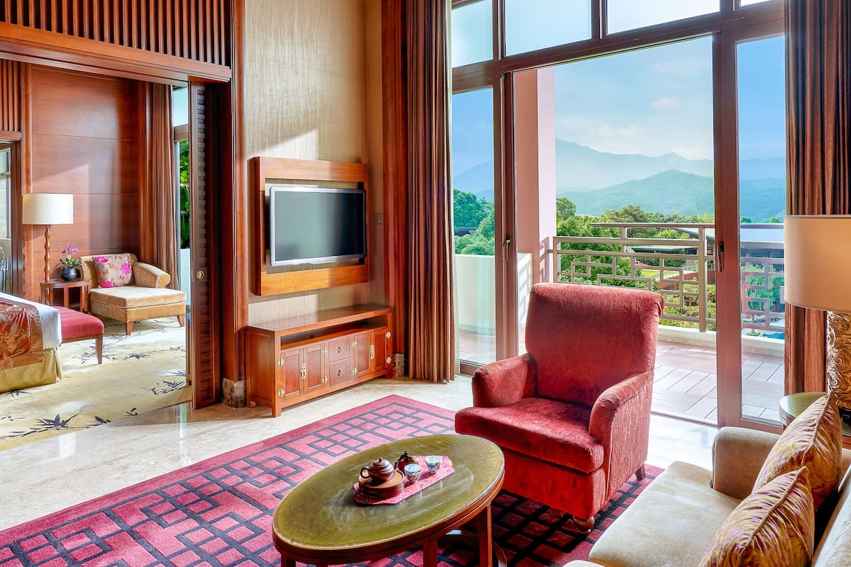 A spacious living room with a large TV, comfortable seating, a red armchair, and a view of mountains through large windows.