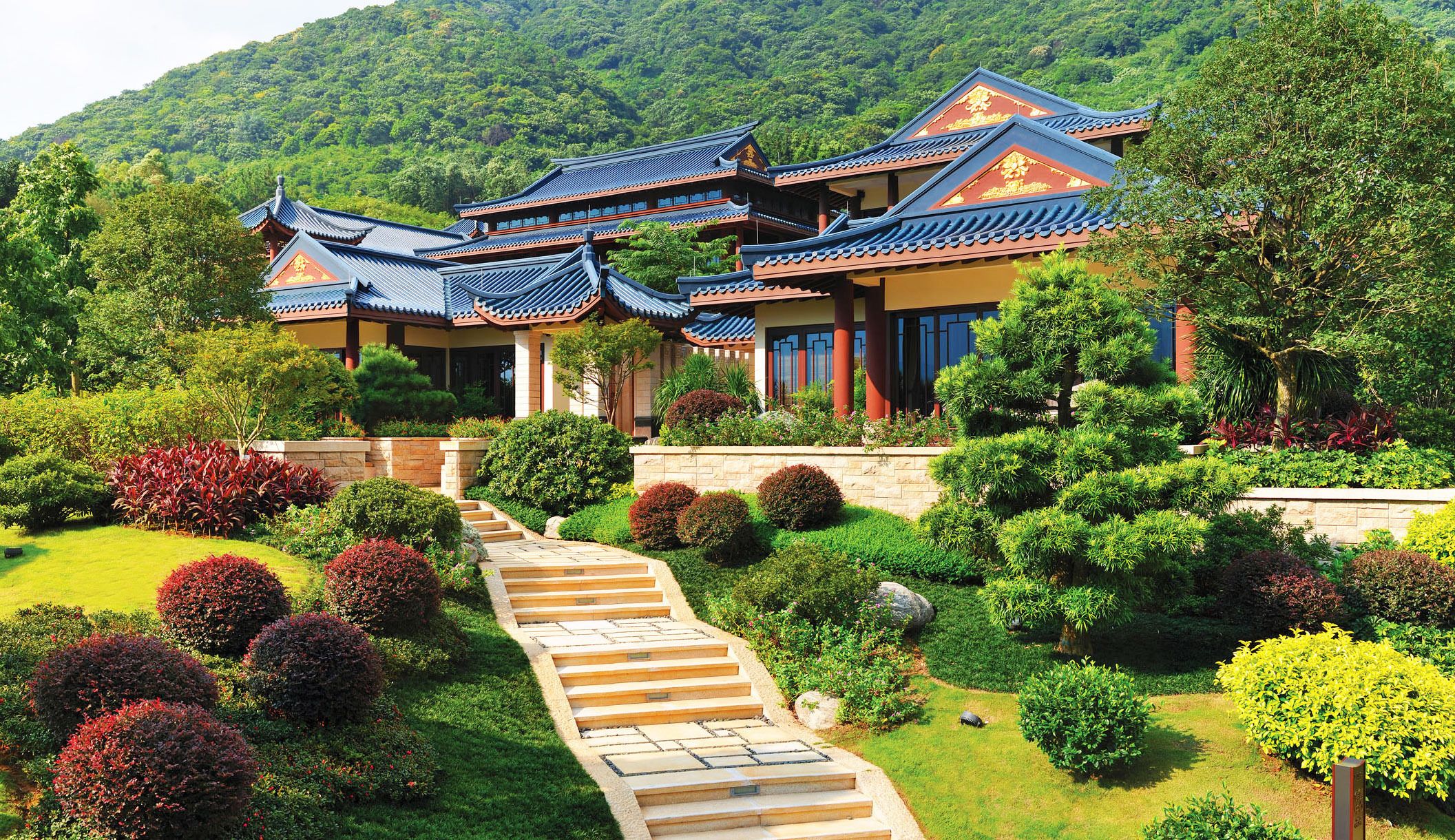 A traditional multi-story building with a tiled roof, surrounded by well-maintained gardens and a stone staircase leading to the entrance.