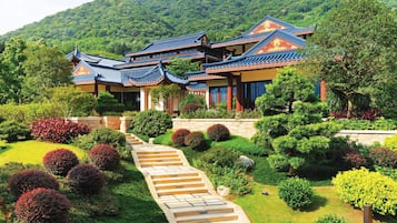 A traditional multi-story building with a tiled roof, surrounded by well-maintained gardens and a stone staircase leading to the entrance.