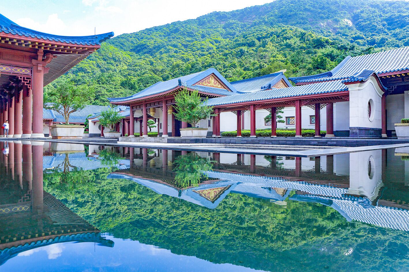 Un edificio de estilo coreano tradicional reflejado en el agua, rodeado de exuberante vegetación y colinas.