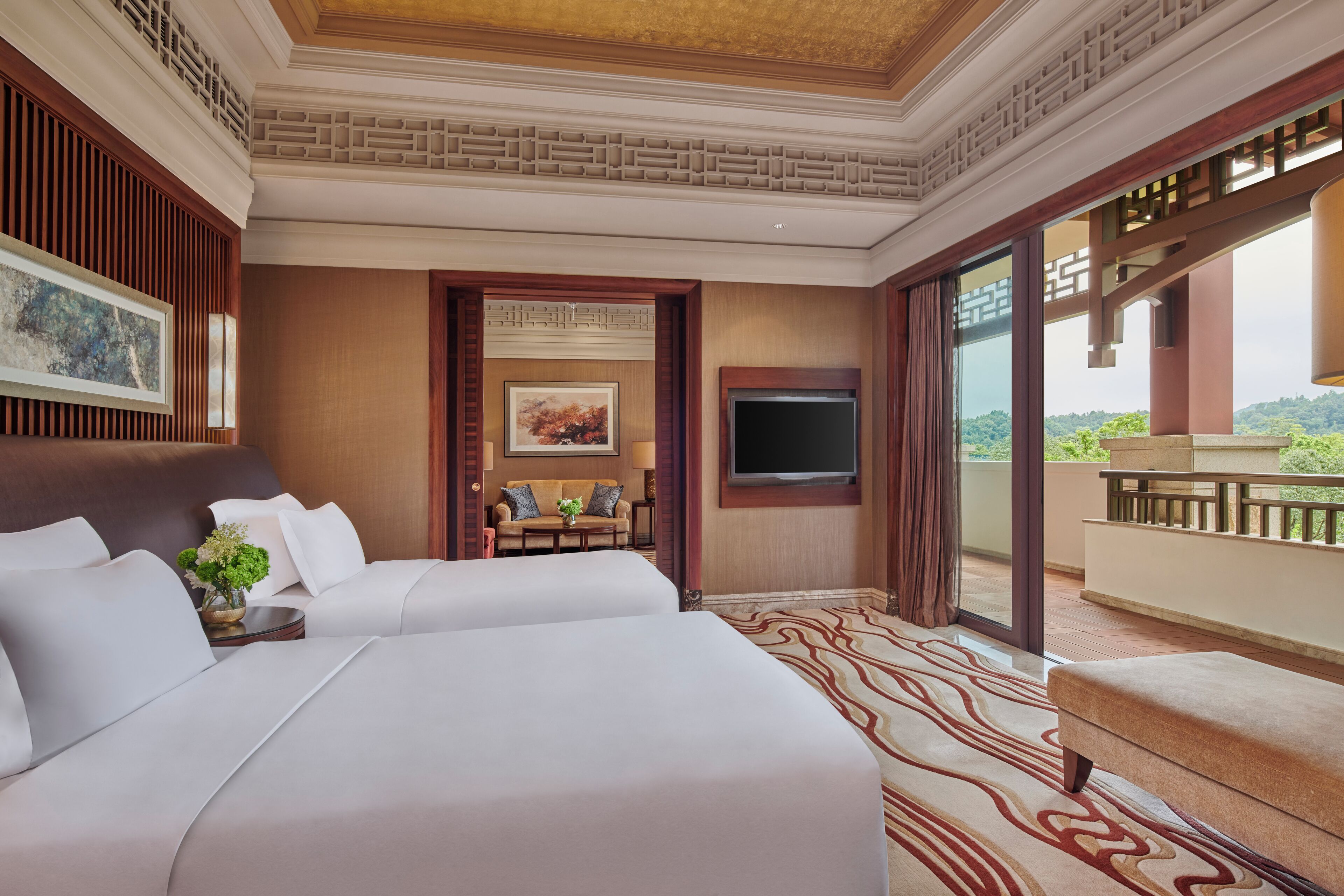 A hotel room with two beds, a flat-screen TV, a sofa, and a balcony with a view.