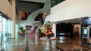 A modern lobby with a central staircase, a reception desk, and a large floral arrangement.