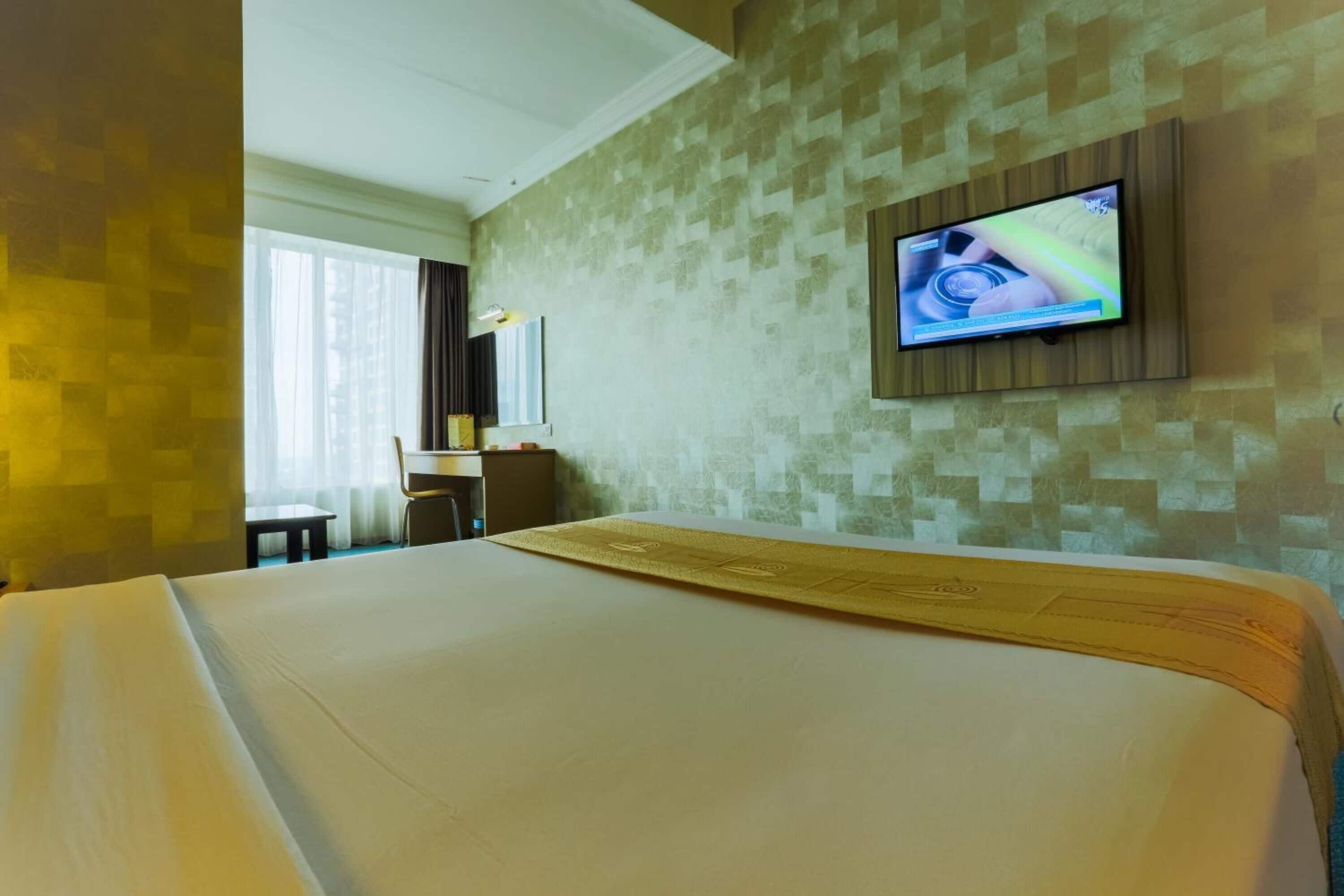 A hotel room with a large bed, a desk, a chair, and a television mounted on the wall.