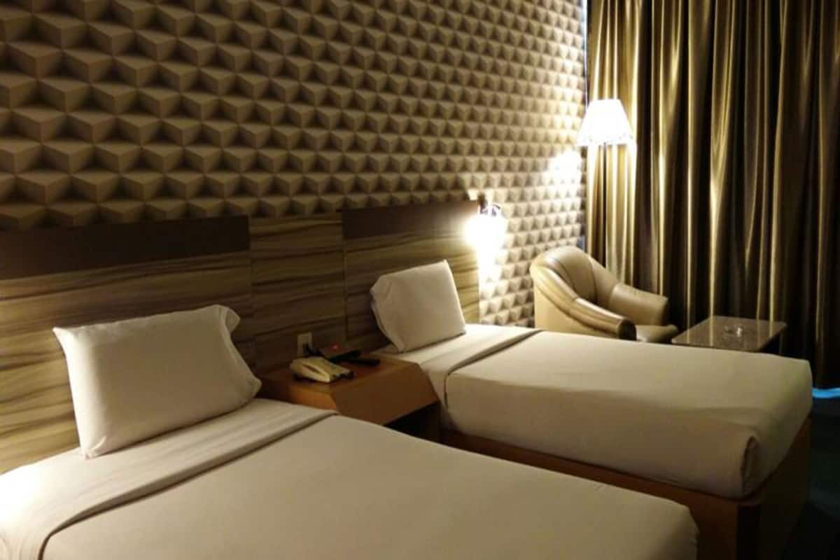 A hotel room with two beds, a headboard with a geometric pattern, a lamp, and a chair.