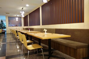 Un amplio comedor con varias mesas y sillas, paneles de madera en las paredes y un árbol de Navidad al fondo.