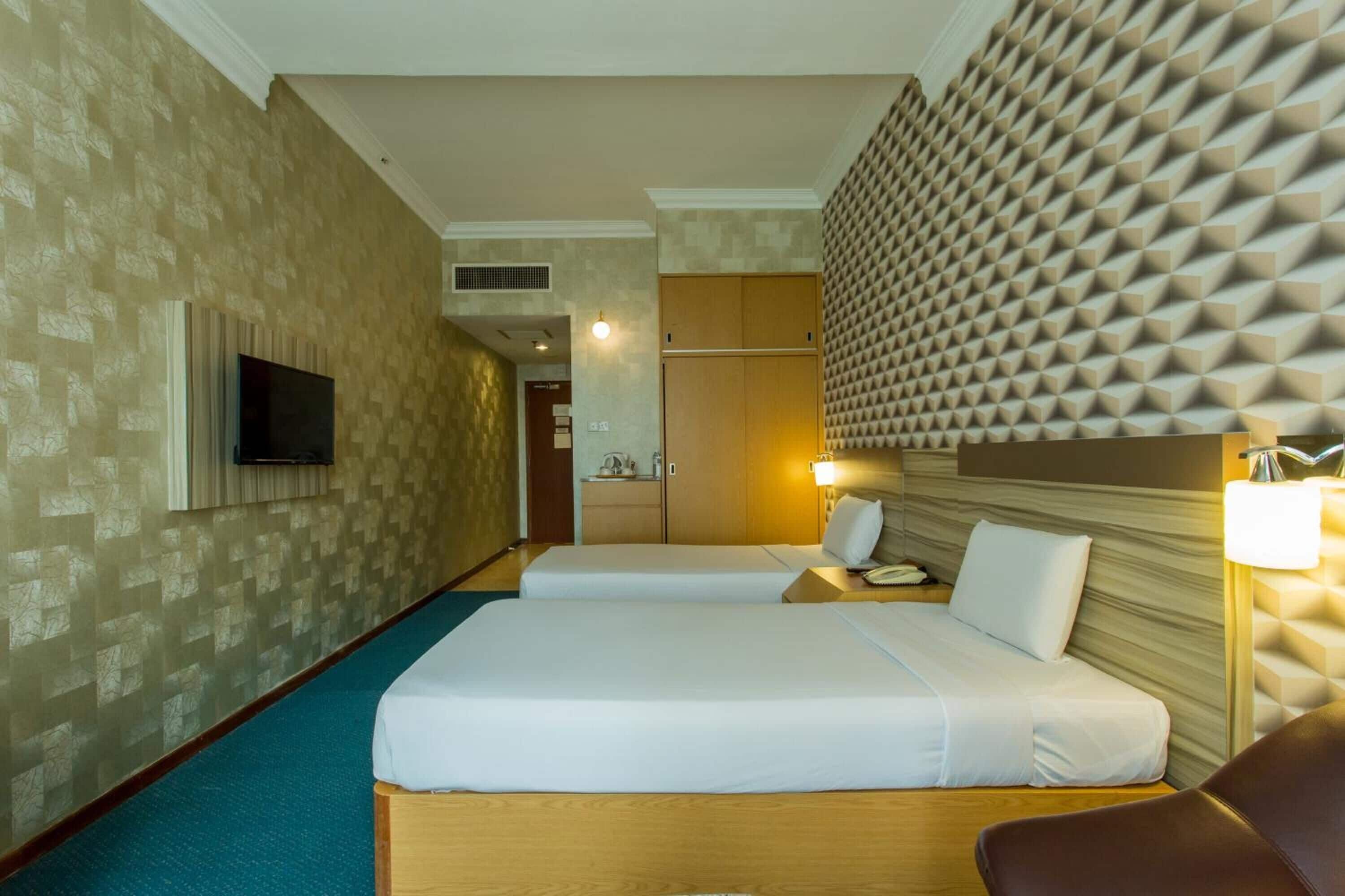 A hotel room with two beds, a TV, a desk, and a wall with a geometric pattern.