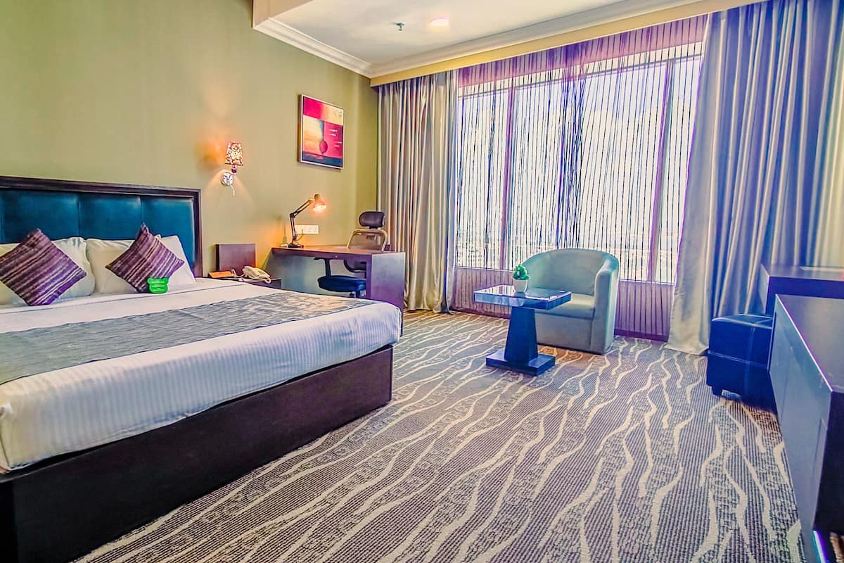 A hotel room with a large bed, a desk, a chair, and a small table.