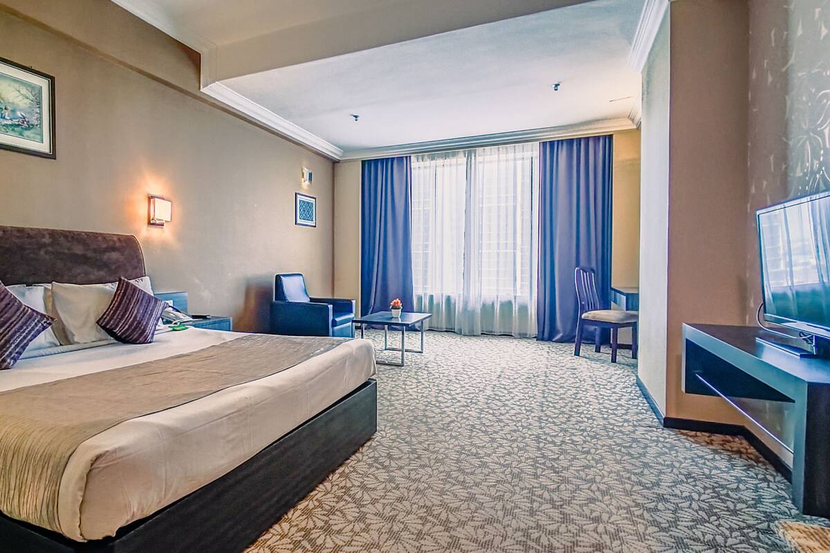 A hotel room with a large bed, a desk, a chair, and a television.