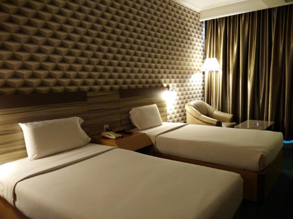 Ett hotellrum med två sängar, en sänggavel, ett nattduksbord, en lampa, en stol och en gardin.