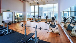 A gym with cardio machines, weightlifting equipment, and a large window with a city view.
