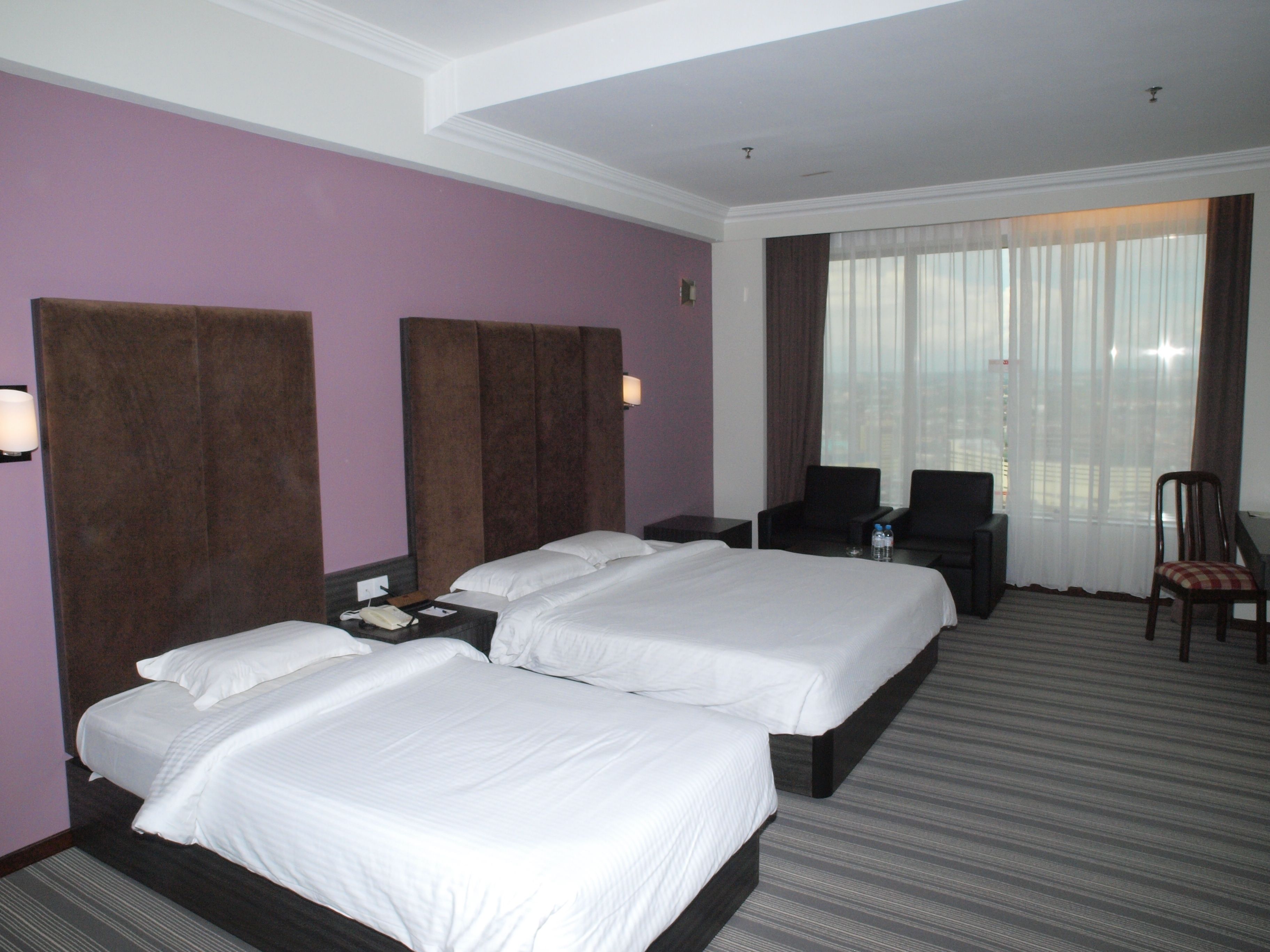 A hotel room with two beds, a desk, a chair, and a large window with curtains.
