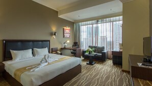 A hotel room with a large bed, a desk, a chair, a television, and a window with curtains.