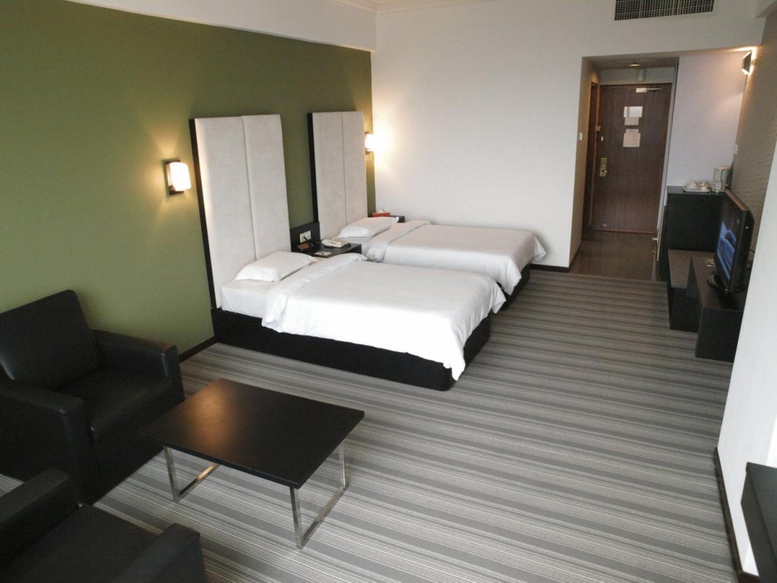 A hotel room with two beds, a sofa, a small table, and a TV.