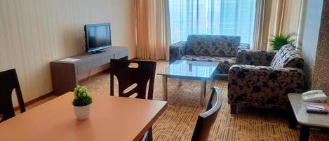 A hotel room with a dining area, a sofa, a TV, and a window with curtains.