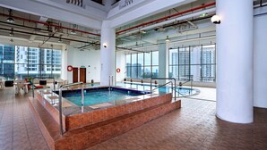 An indoor swimming pool with clear glass walls, a tiled floor, and a view of high-rise buildings.