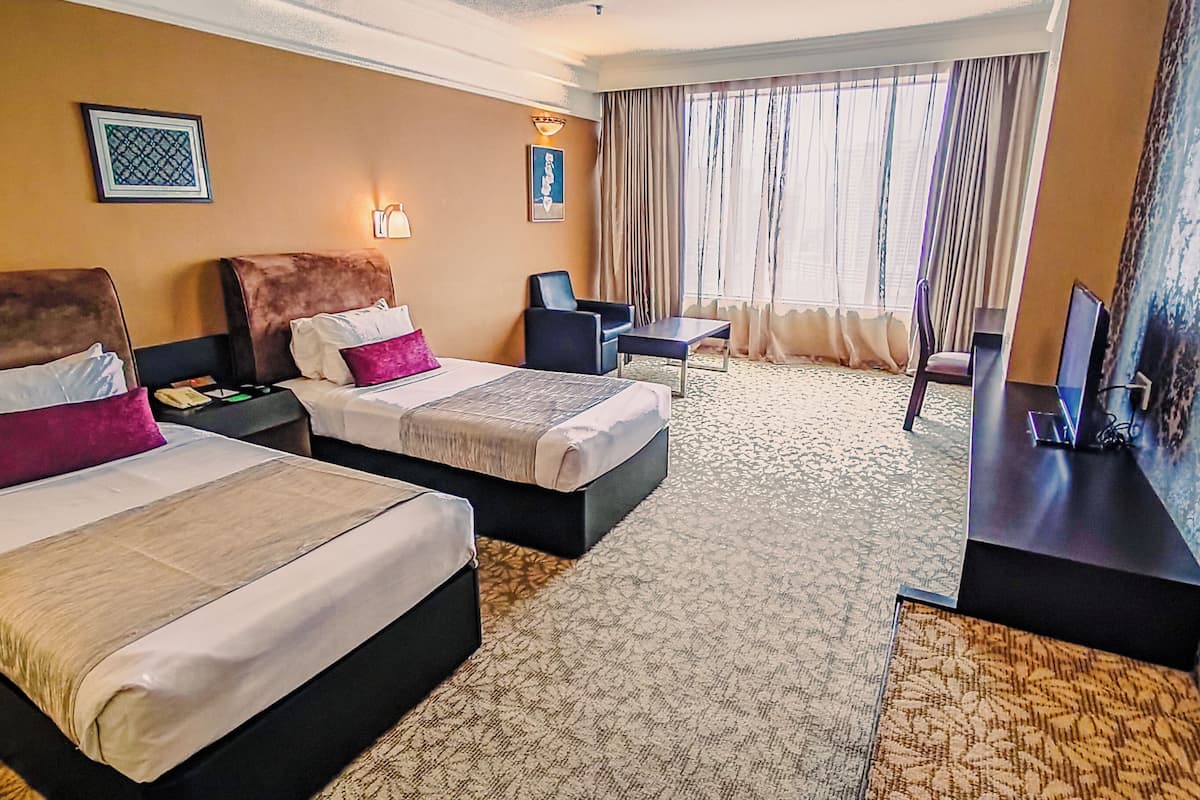 A hotel room with two beds, a desk, a chair, a TV, and a window with curtains.