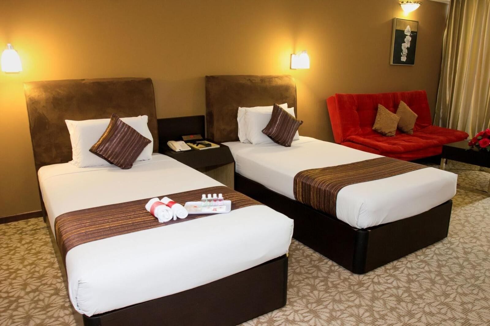 A hotel room with two beds, a red armchair, and a nightstand with a phone.