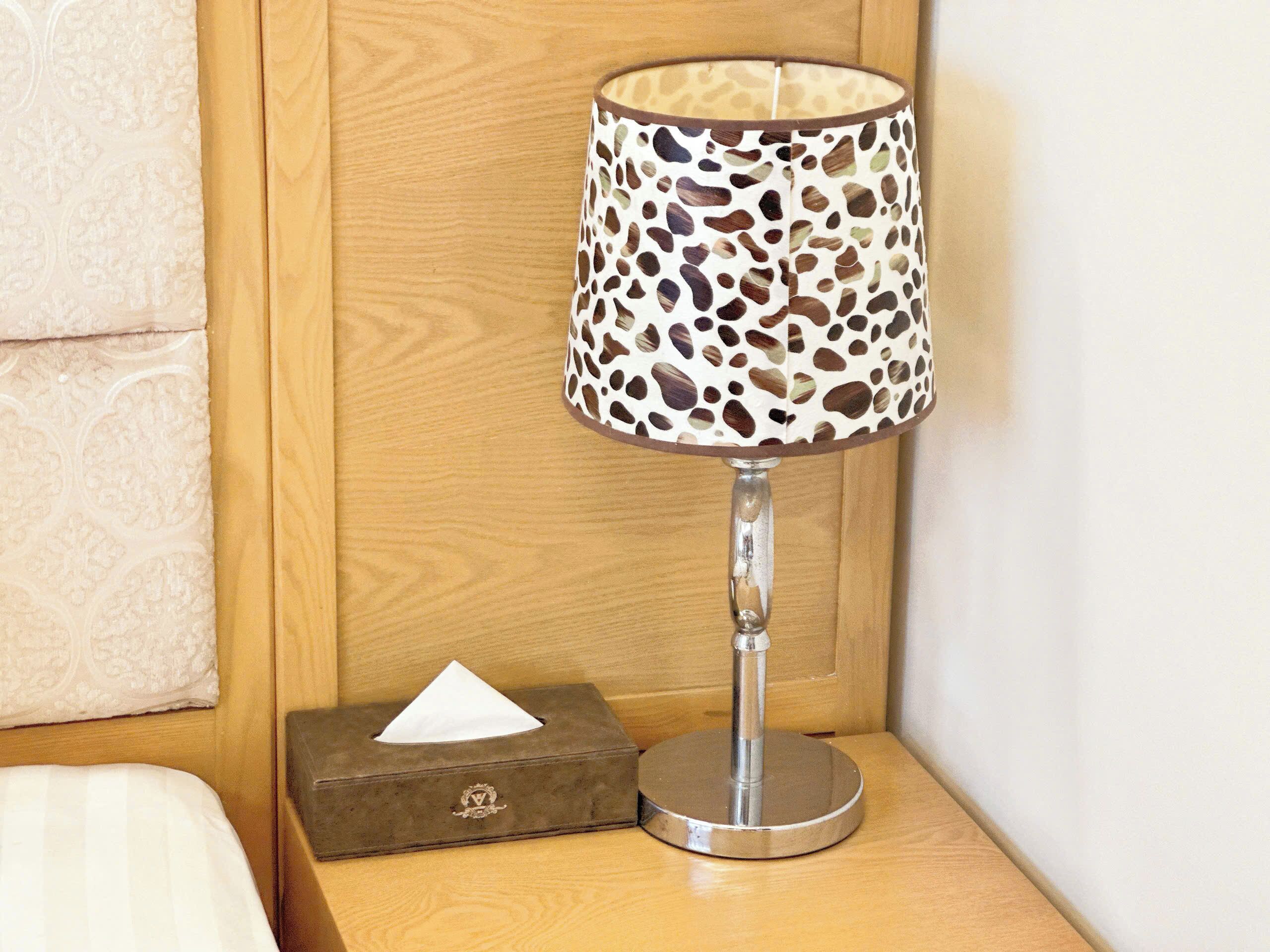 Una mesita de noche con una lámpara de pantalla estampada con diseño de leopardo, una caja de pañuelos y un tocador de madera.