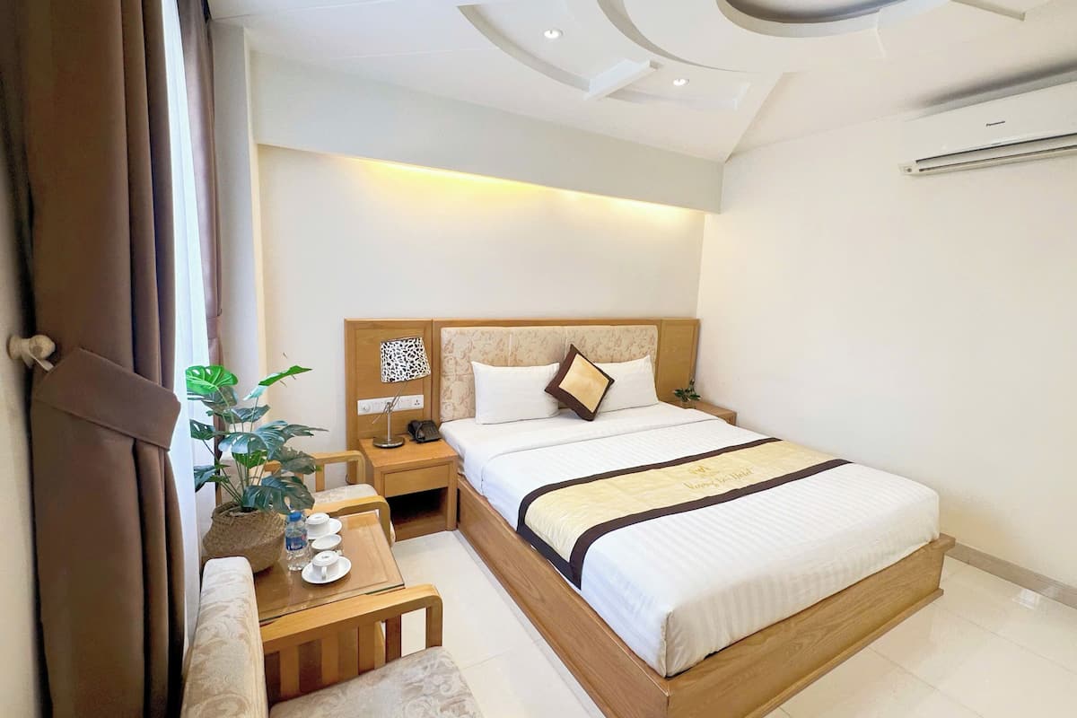 Habitación de hotel con cama, mesita de noche, lámpara y un pequeño rincón de descanso.