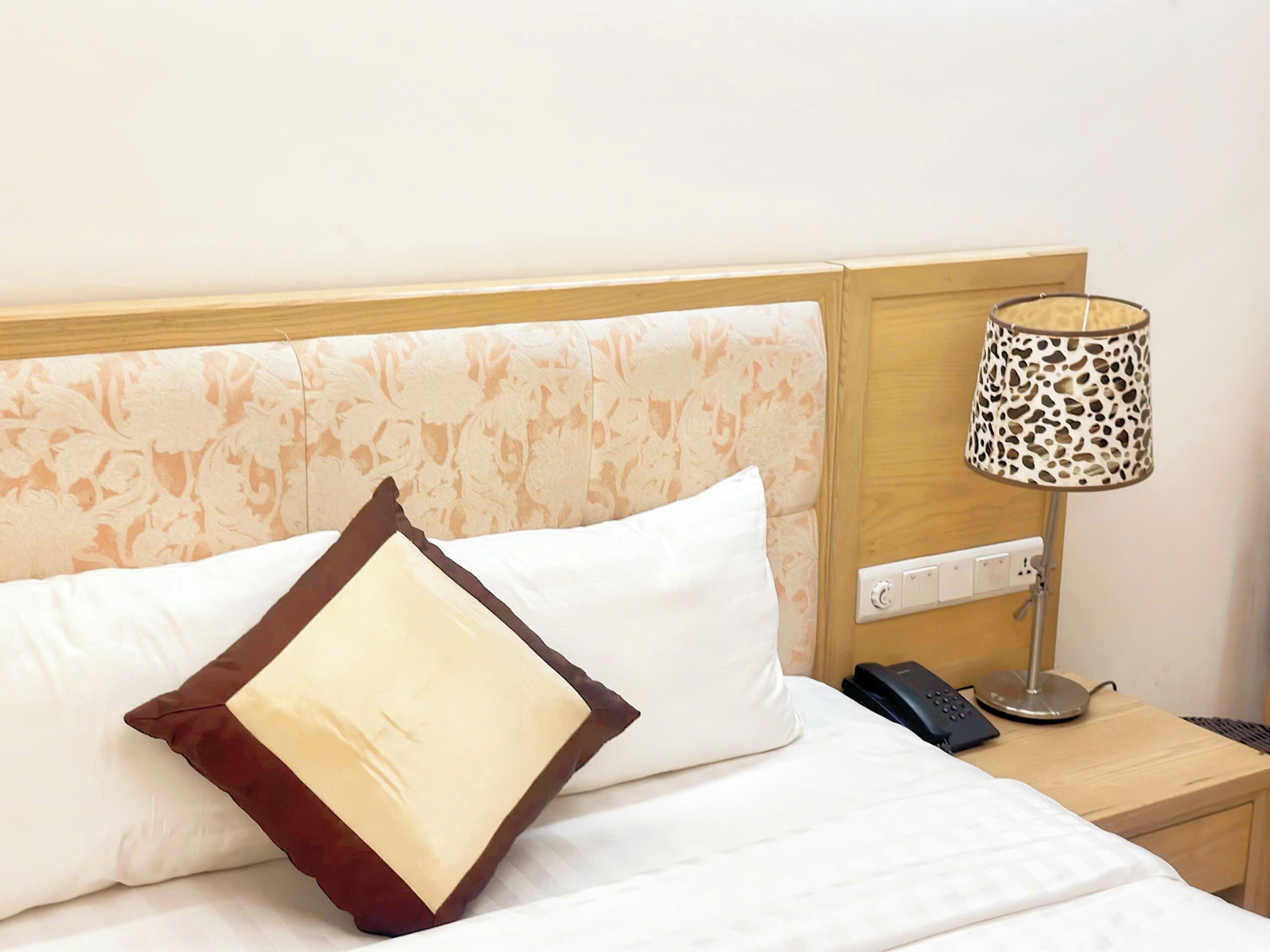 Habitación de hotel con cama, mesita de noche, lámpara y teléfono.
