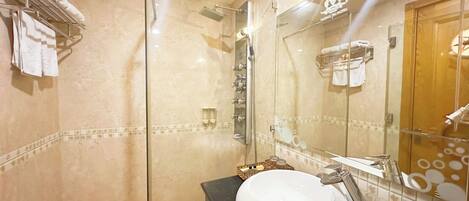 A bathroom with a glass-enclosed shower, a white sink, and a mirror reflecting a towel rack and a wooden door.
