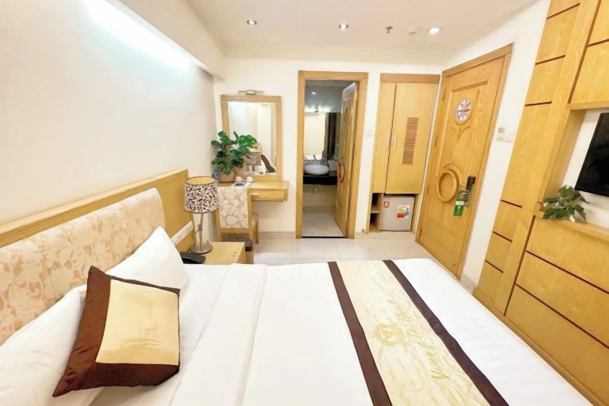 Habitación de hotel con cama, mesita de noche, lámpara, espejo, armario y vistas al baño.